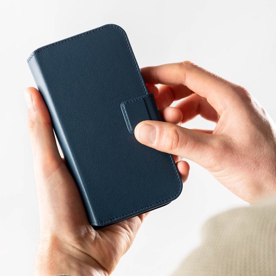 Handen houden een gesloten donkerblauwe lederen bookcase telefoonhoes vast.