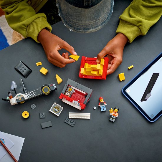 Kind bouwt LEGO snackbartruck met tablet. Rode en gele elementen, plus mini-figuurtjes.