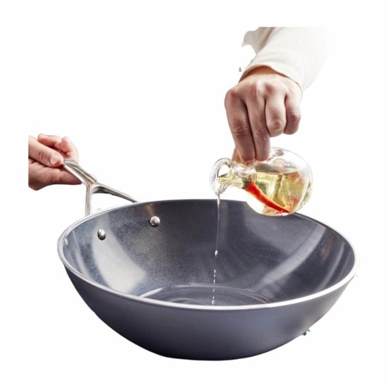 Persoon voegt olie met pepers toe aan een wokpan.
