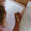 Kind met blonde vlecht tekent prinses op roze lichttablet, met potlood.