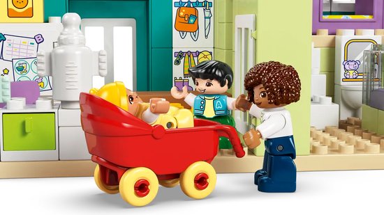 Figurines Duplo, dont un bébé dans un chariot rouge, près d'une cuisine avec réfrigérateur.