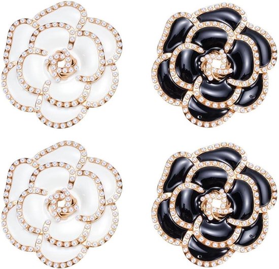 Vier bloemvormige broches in zwart en wit met gouden randen en kleine witte kristallen.