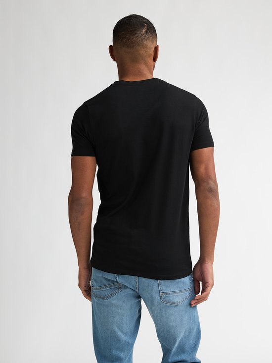 Man met donkere huid, draagt een zwart V-hals T-shirt en lichtblauwe jeans, gezien vanaf de achterkant.
