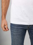 Onderlichaam van een man die een wit T-shirt en een spijkerbroek draagt.