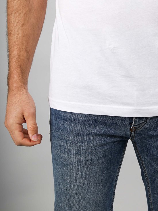 Onderlichaam van een man die een wit T-shirt en een spijkerbroek draagt.