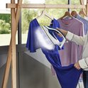Een vrouw stoomt een blauwe jurk met de witte en donkerblauwe Tefal Pro Express Ultimate II stoomstrijkijzer.