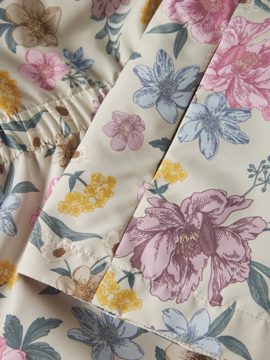 Detail van beige jas met opgestikte zakken en bloemenprint.