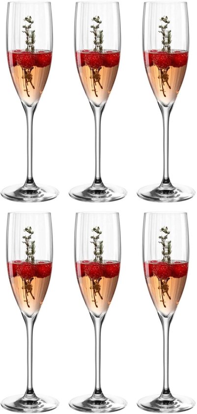 Zes champagneglazen met verticale ribbels, elk gevuld met champagne, frambozen en takjes.