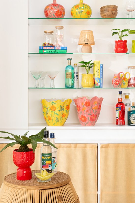 Vases jaune et corail à bord ondulé, décorés de fleurs et de feuilles, posés sur une étagère blanche.