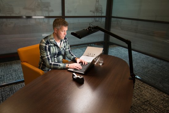 Man in geruit overhemd werkt aan laptop met bureaulamp.