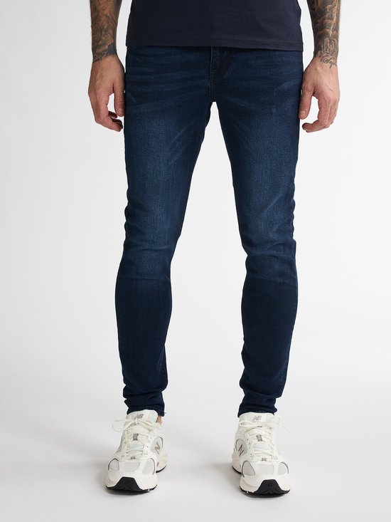 Voeten van een man in een blauwe skinny jeans en witte New Balance sneakers.