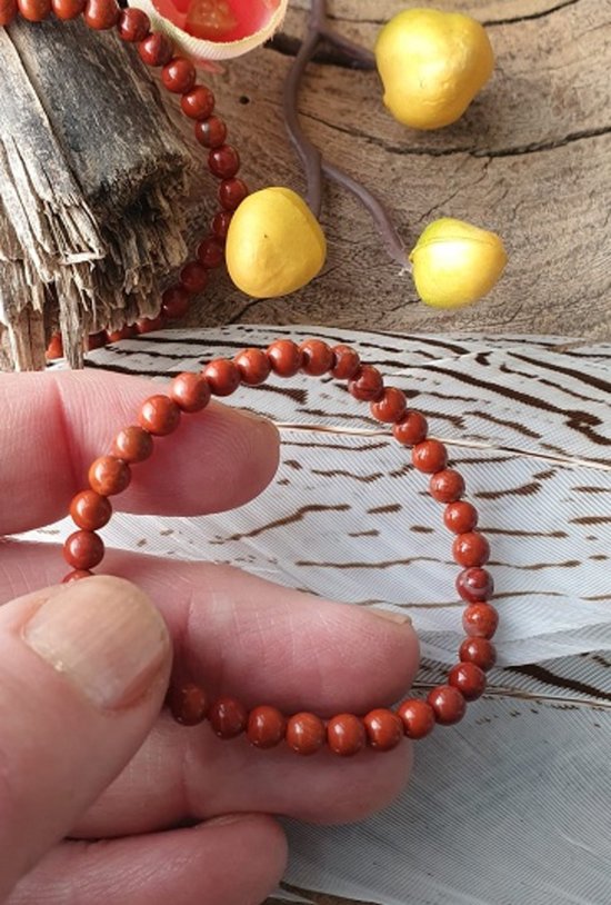 Een rood jaspis kinderarmbandje van 4 mm, met kralen, vastgehouden in een hand.