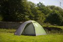 Grijze en groene Coleman Darwin 3 koepeltent met open tentdeur, opgesteld op gras met bomen op de achtergrond.