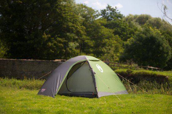 Grijze en groene Coleman Darwin 3 koepeltent met open tentdeur, opgesteld op gras met bomen op de achtergrond.
