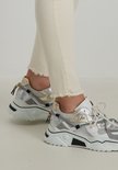 Close-up van beige skinny jeans met rafelige zoom en zilverkleurige sneakers met veters.