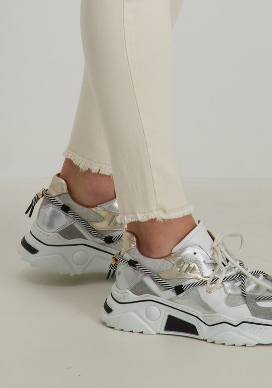 Close-up van beige skinny jeans met rafelige zoom en zilverkleurige sneakers met veters.