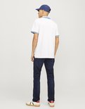 Man draagt een donkerblauwe jeans en een witte polo met blauwe kraag en mouwranden, met blauwe pet.