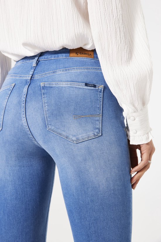 Close-up van achterzak van blauwe Garcia jeans met logolabel, gedragen met wit overhemd.
