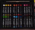 Gedetailleerde weergave van 24 oliepastels, georganiseerd per kleur in een kunstenaars koffer.