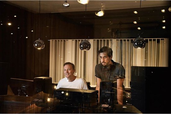 Twee mannen in een studio, de rechtse draagt een zwarte koptelefoon.