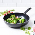 Zwarte wokpan met broccoliroosjes, peultjes en radijzen. Groene pan met wit handvat.