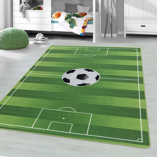 Een groen kleed met voetbalveldprint, met een zwart-wit voetbal in het midden, in een kinderkamer.