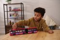 Jongen speelt met rode dubbele stadsbus op houten tafel. De bus heeft 'ELECTRIC CITY LINE' en blauwe cirkels.