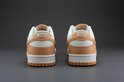 Achterkant van een paar Nike Dunk Low damesschoenen, wit met oranje overlays en 'NIKE' op de hiel.