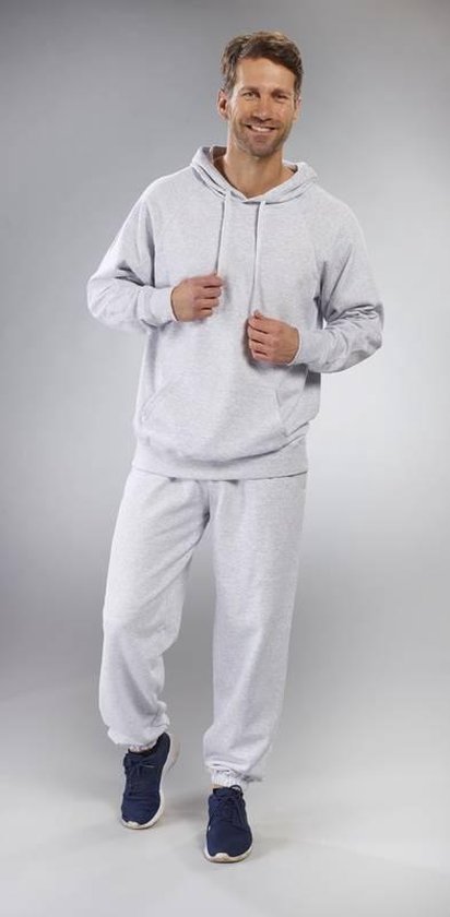 Man draagt een lichtgrijze hoodie met capuchon en een lichtgrijze joggingbroek. Handen in de zakken.