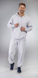 Man draagt een lichtgrijze hoodie met capuchon en een lichtgrijze joggingbroek. Handen in de zakken.