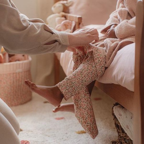 Une personne aide un enfant à enfiler un pantalon de pyjama à fleurs, gros plan sur les jambes.