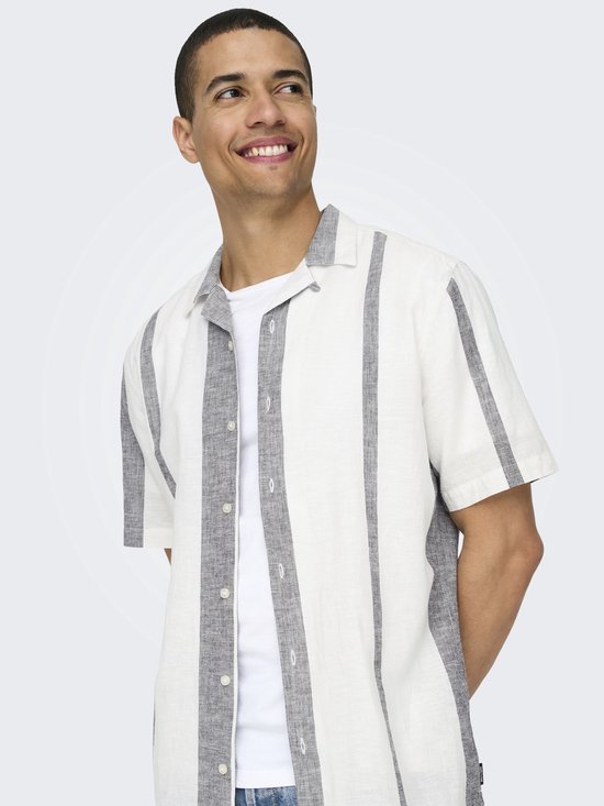 Man met een lachend gezicht, draagt een wit kort-mouw overhemd met verticale grijze strepen. Wit T-shirt eronder.