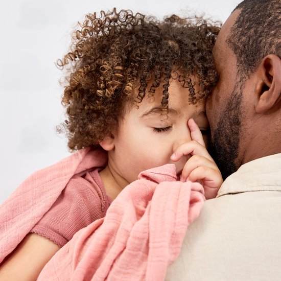 Kindje slaapt op de schouder van een man, gewikkeld in een zachtroze swaddle.