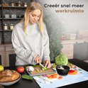 Een vrouw snijdt komkommer op een snijplank, naast een inductiebeschermer met een print van bloemen.