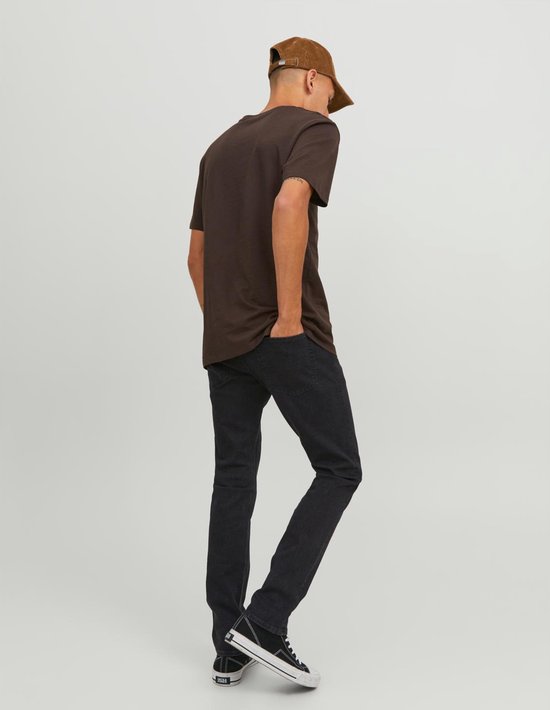 Man in zwarte jeans en bruine T-shirt, kijkend naar achteren.