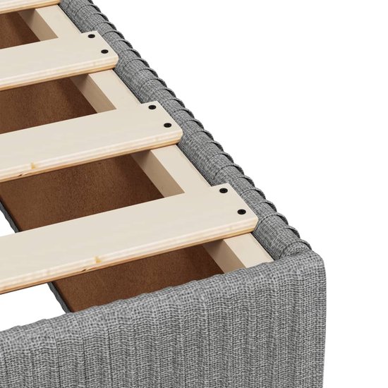 Gros plan du bord textile gris clair d'un sommier à lattes en bois.