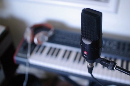 Zwarte sE X1 A microfoon op een microfoonstandaard, in de buurt van een keyboard en koptelefoon.