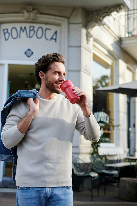 Homme buvant d'une tasse rose dans ses mains à l'extérieur.