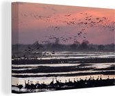 Canvas schilderij 180x120 cm - Wanddecoratie Kraanvogels vliegen boven het water met een oranje lucht in Nebraska - Muurdecoratie woonkamer - Slaapkamer decoratie - Kamer accessoires - Schilderijen