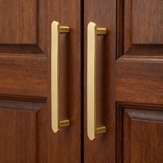 Twee matte messing handgrepen met gouden kleur op houten kasten.