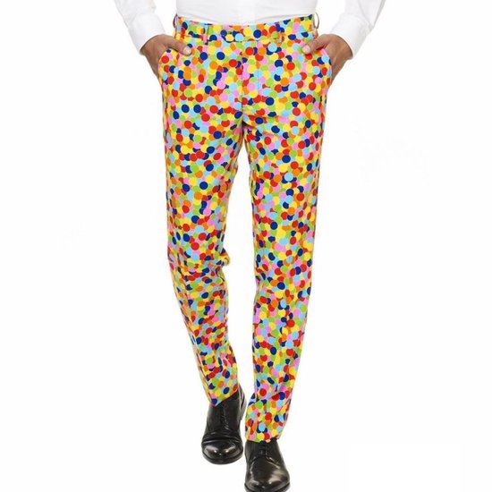 Man met de handen in de zakken, draagt een broek met confettiprint en zwarte schoenen.