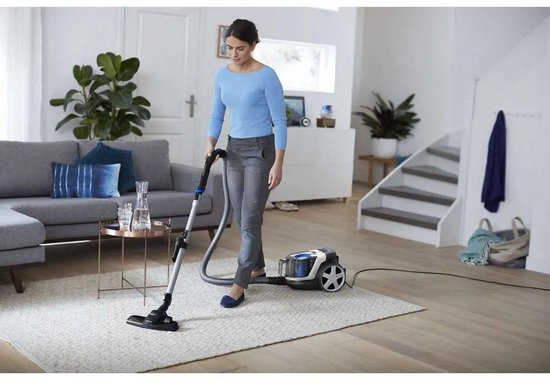 Femme en pull bleu aspirateur un salon avec aspirateur blanc.