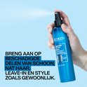 Hand spuit blauwe fles Redken Extreme Anti-Snap leave-in treatment op lichtblauwe achtergrond.