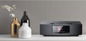 Zwarte Kenwood radio op een witte plank, naast gouden en zwarte decoratieve vazen met witte bloemen.