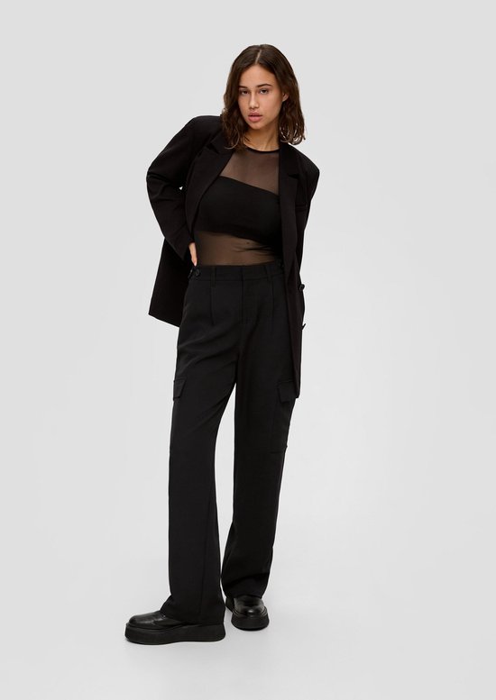 Model draagt een zwarte cargobroek, een zwarte mesh-top en een bijpassende zwarte blazer.