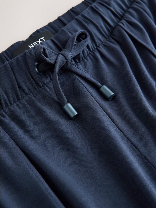 Close-up van de donkerblauwe joggingbroek met trekkoord, knopen en Next label.