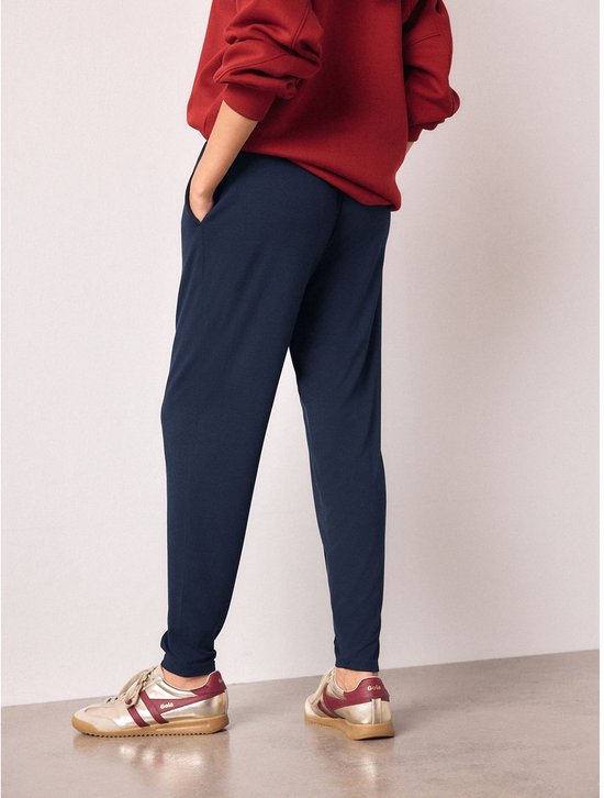 Donkerblauwe joggingbroek met trekkoord en zakken, gedragen door een model met een rode sweater en gouden sneakers.