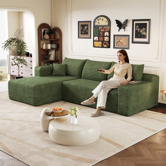 Vrouw zit op een groene ribstof hoekbank met chaise longue, met afstandsbediening.
