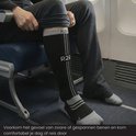 Zwarte compressiekousen met grijze accenten en 'R2B' logo, gedragen door een man zittend op een vliegtuigstoel.