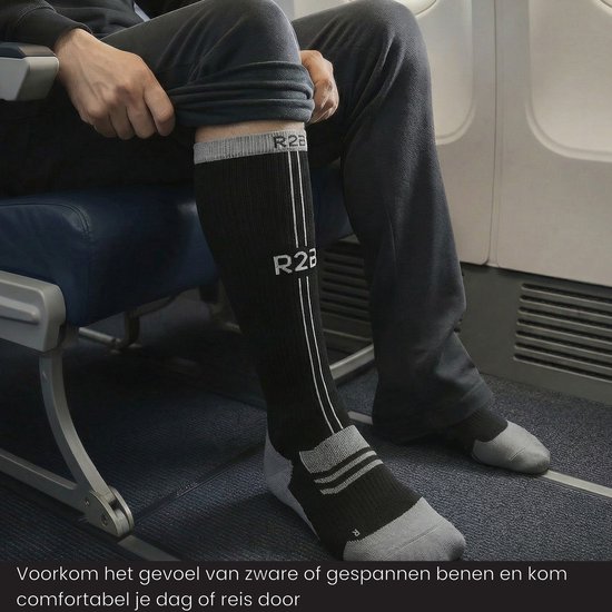Zwarte compressiekousen met grijze accenten en 'R2B' logo, gedragen door een man zittend op een vliegtuigstoel.